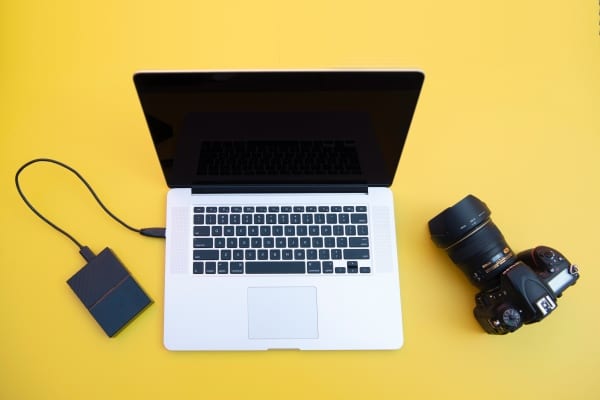 a camera next to a laptop with an external hard drive connected via USB cord