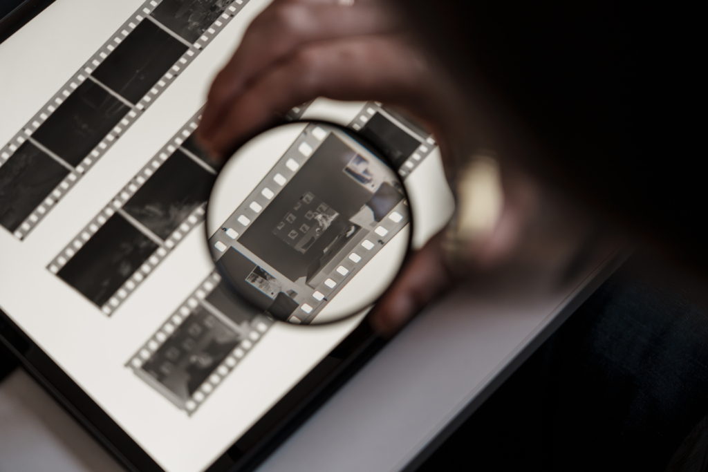 Close-up of a person's hand analyzing film negatives on a lightbox using a magnifying glass to inspect details.