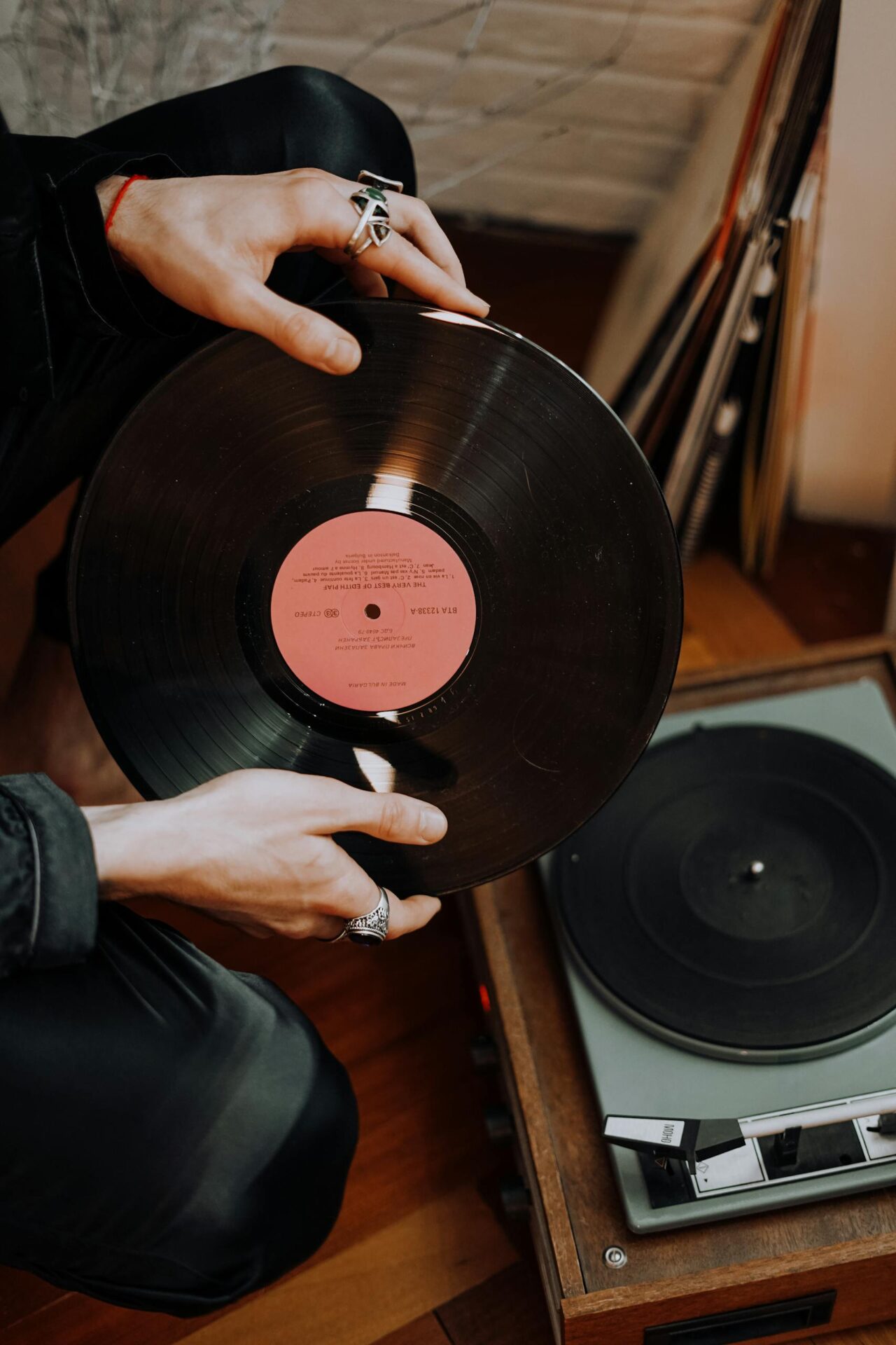 Close-up of hands with rings holding a classic vinyl record above a retro player.