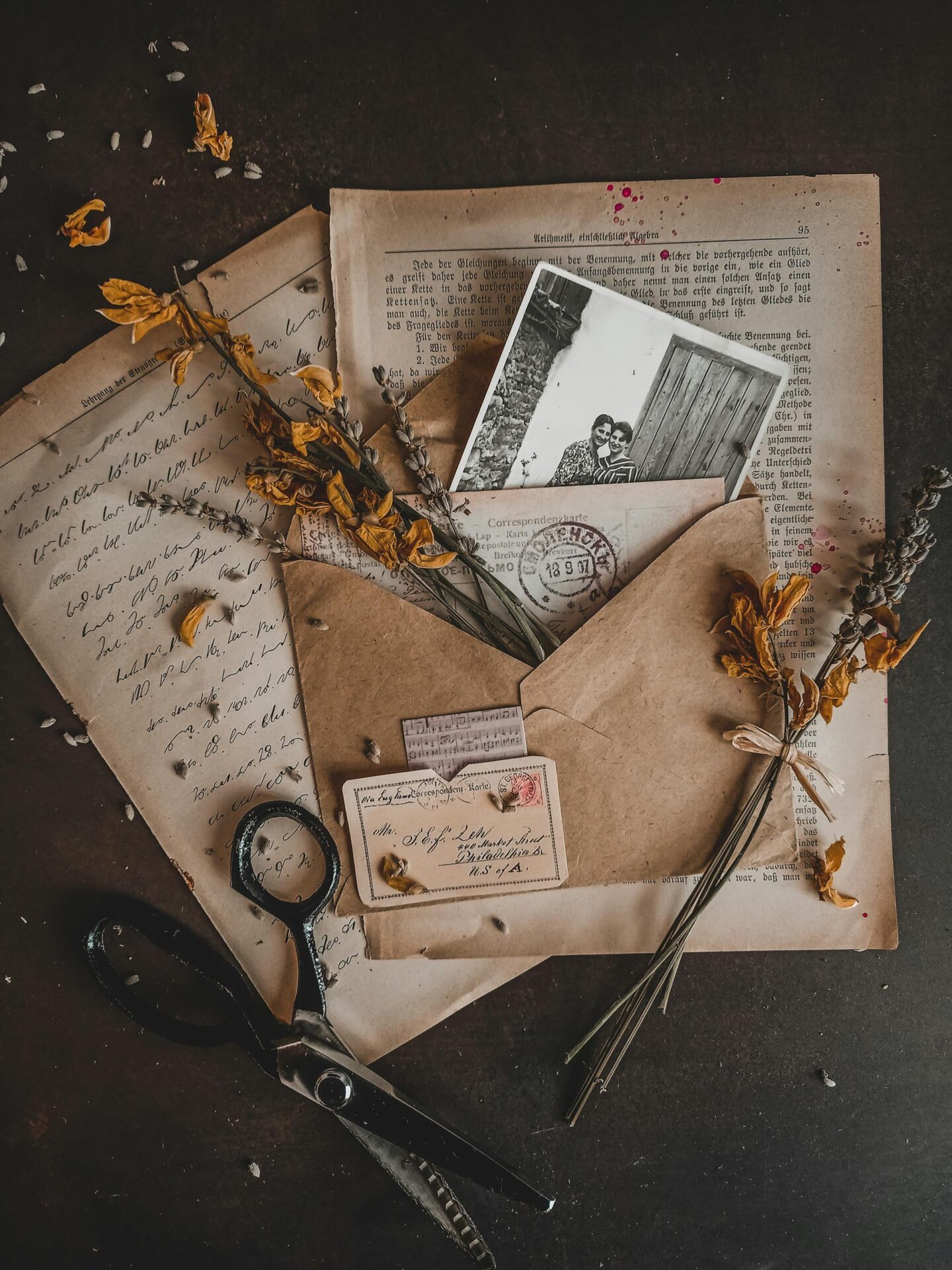 Charming vintage arrangement with dry flowers, envelopes, and old photographs in a rustic setting.