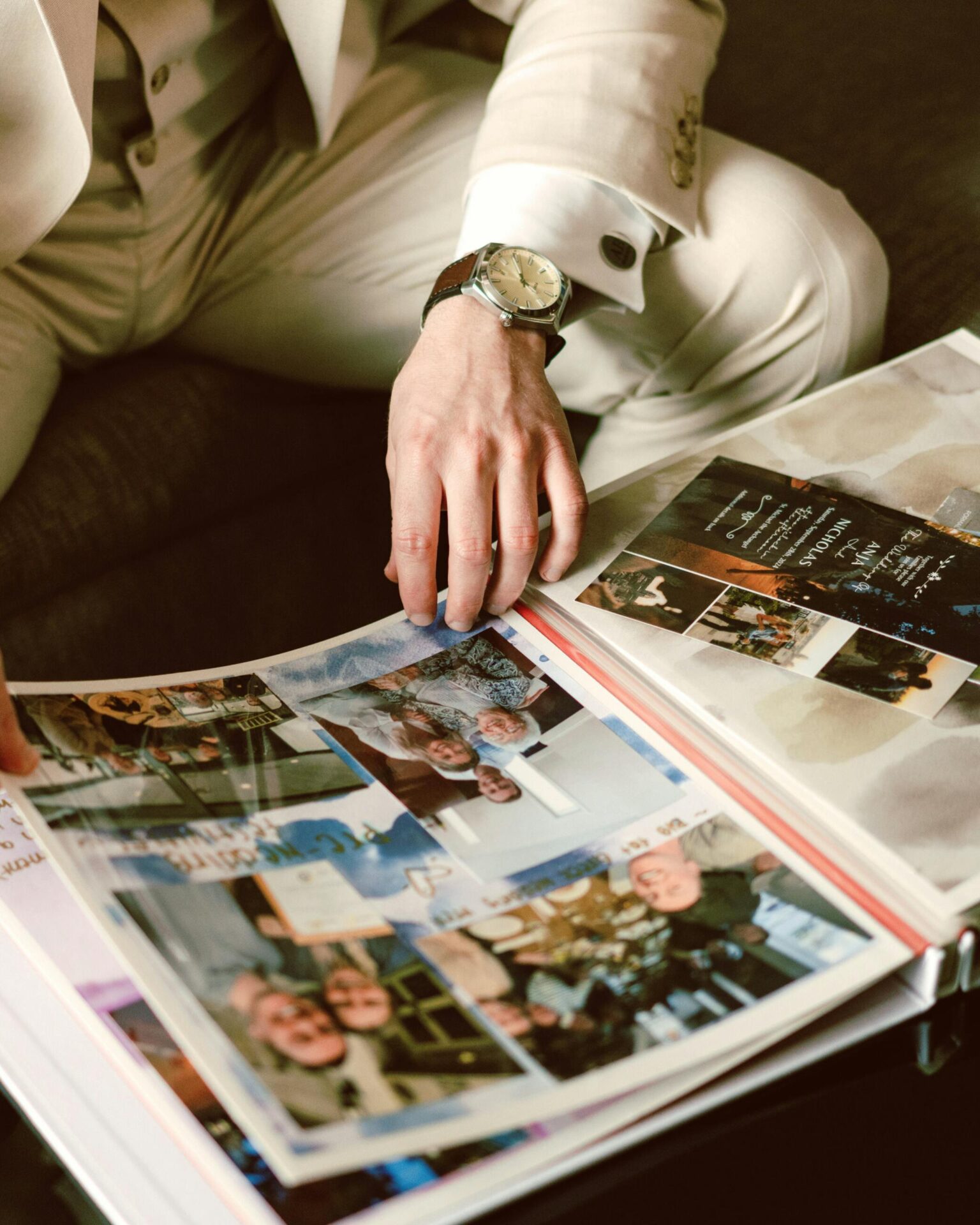 Man in beige suit looking through a photo album, capturing precious memories.